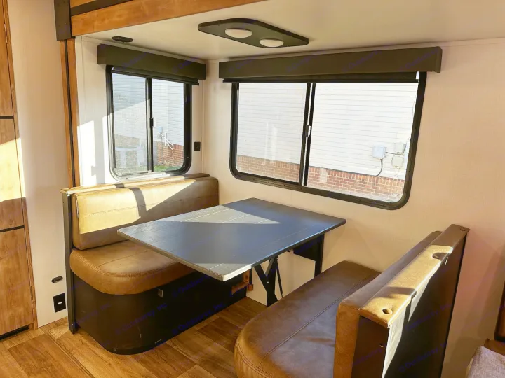 Bright RV rental dinette featuring a table, two upholstered benches, and large windows, ideal for meals or work.. Keystone RV Outback Toy Hauler 2023