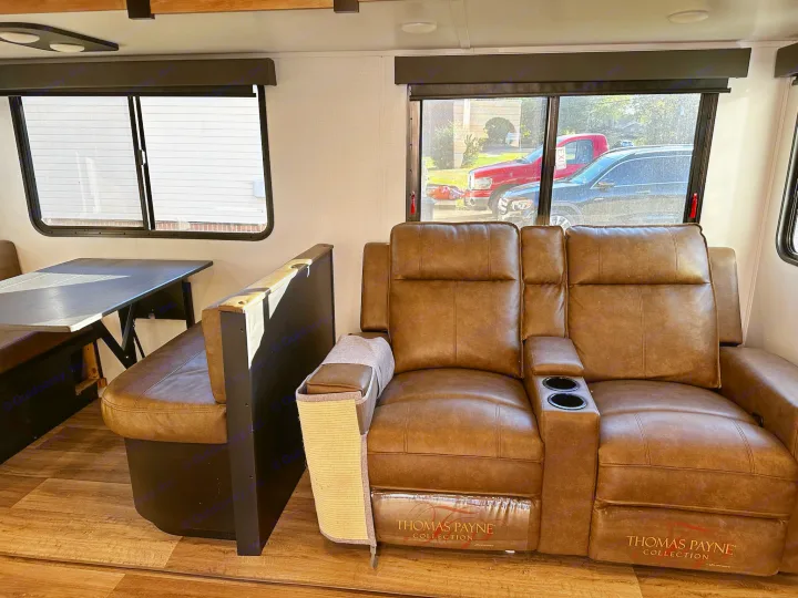 Inside an RV rental: a dining booth on the left, and brown leather recliners with cup holders on the right.. Keystone RV Outback Toy Hauler 2023