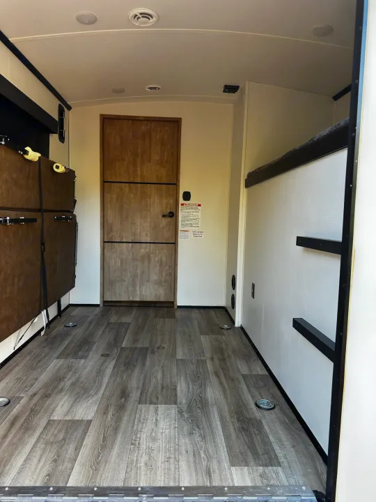 Spacious RV rental interior with fold-down bunks, wood-look floor with tie-downs, and a rear door. Ideal for cargo & sleeping.. Keystone RV Outback Toy Hauler 2023