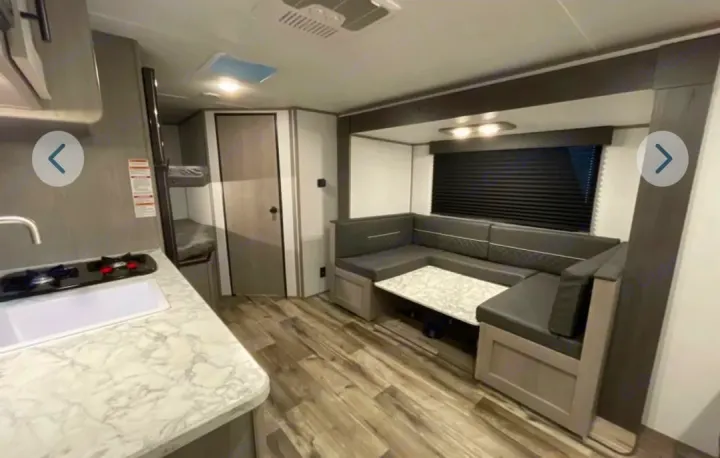 Modern RV rental interior: well-lit kitchen, comfortable U-shaped dinette, and bunk beds in the back. Ready for your trip.. Dutchmen Coleman Lantern Lt 19BB 2024