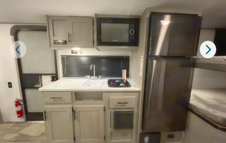 This RV rental features a modern kitchen setup with fridge, microwave, sink, stovetop, & nearby bunk beds.. Dutchmen Coleman Lantern Lt 19BB 2024