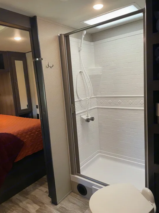 Inside an RV rental: a bright, compact bathroom with a shower, toilet, and an inviting view of the adjacent bedroom.. Grand Design Transcend 2021