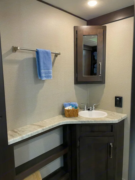 This RV rental bathroom features a dark wood vanity, sink, mirror, and blue towels on a light textured wall.. Grand Design Transcend 2021