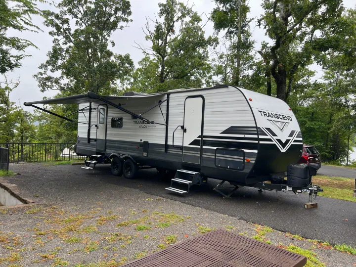 Grand Design Transcend Xplor RV rental parked at a wet, wooded campsite with an extended awning and a lake view.. Grand Design Transcend 2021