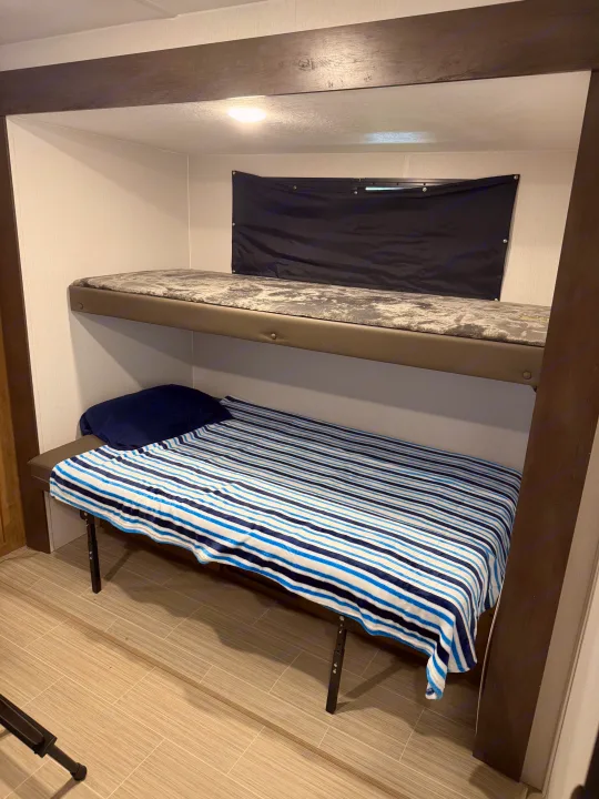 Compact sleeping area in an RV rental, featuring comfortable bunk beds with a striped blanket below and grey mattress above.. Coachmen Express 2024
