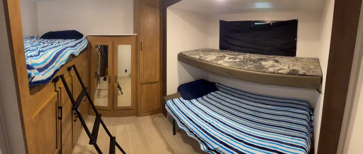 This RV rental interior features multiple bunk beds, a ladder, blue and white striped bedding, and mirrored storage.. Coachmen Express 2024