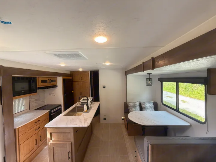 Inside a bright RV rental: a sleek kitchen with an island and modern appliances, plus a cozy dinette dining area.. Coachmen Express 2024