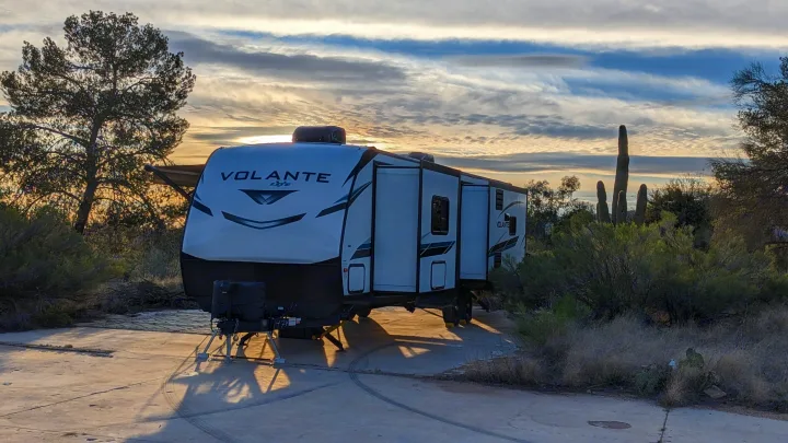 An RV rental travel trailer awaits adventure at a desert campsite under a scenic sunset sky.. Crossroads RV Volante 2022