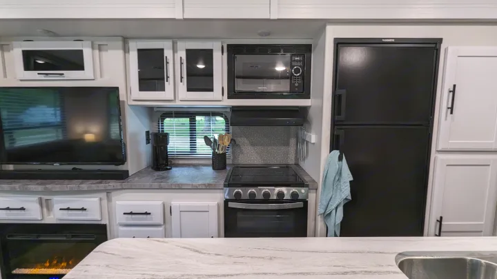 Well-equipped RV rental interior with black appliances, white cabinetry, TV, fireplace, and compact kitchenette.. Crossroads RV Volante 2022