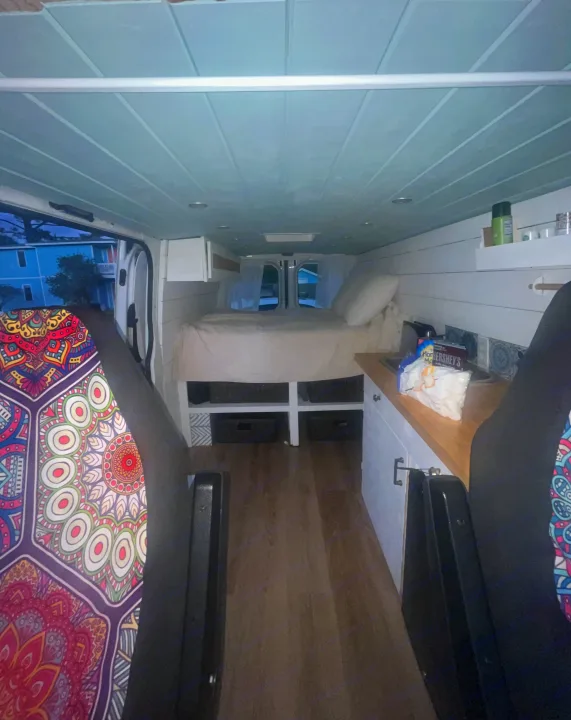 Inside a custom RV rental: light blue ceiling, wood floor, rear bed, and side kitchen with colorful seat details.. Dodge Sprinter Van 2008
