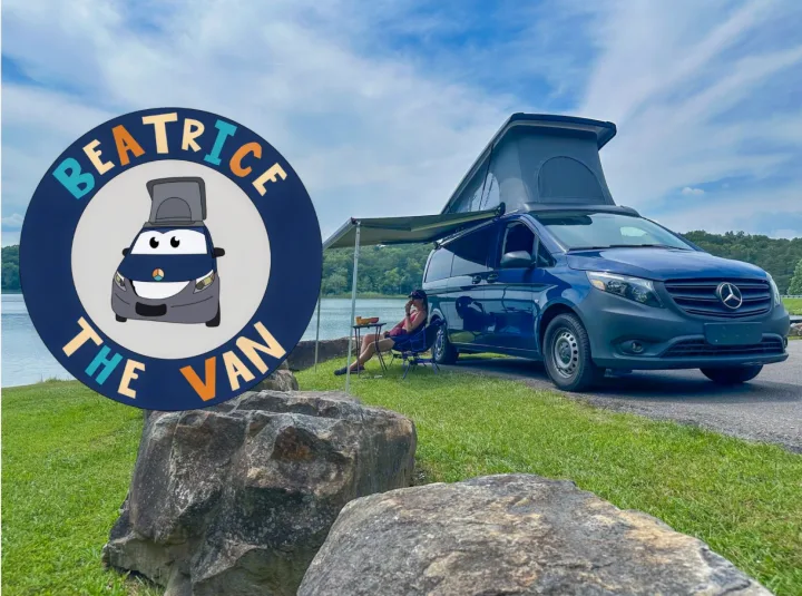 Blue Mercedes-Benz pop-top camper van with awning by a lake, person relaxing. Check out this RV rental, Beatrice the Van!. Mercedes-Benz Metris 2023