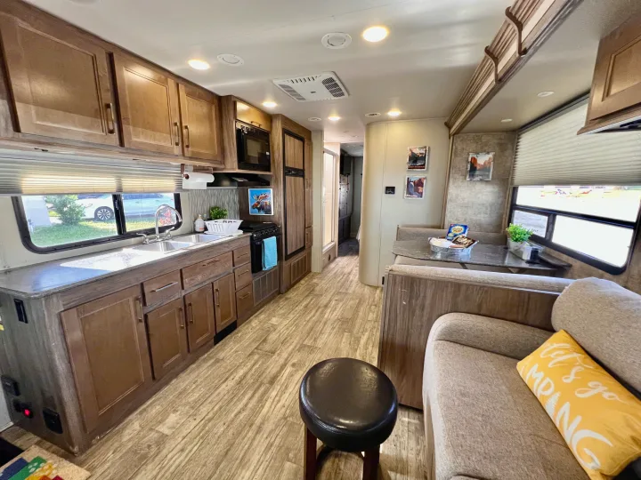 Inside a cozy RV rental: full kitchen, dinette, and living area with wood-look flooring. Great for road trips!. Jayco Envoy 100 2018