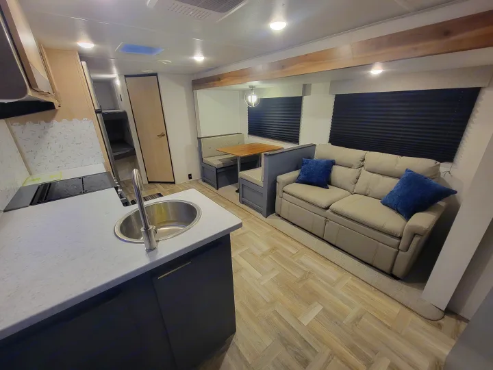 RV rental: Modern interior featuring a kitchen, dinette, sofa with blue pillows, and bunk bed access.. Prime Time Tracer 2700BHSLE 2024