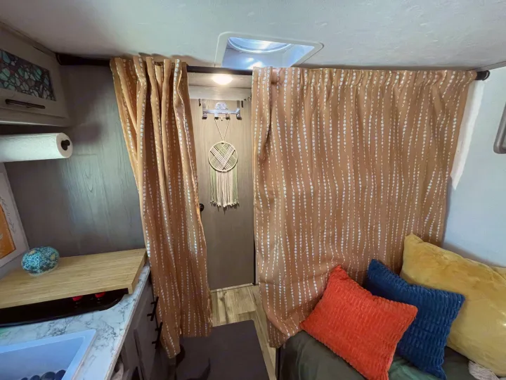 Inviting rv rental interior with tan patterned curtains separating the kitchenette from a comfy bed/lounge area with bright pillows.. Keystone RV COLEMAN LANTERN LT 17B 2024