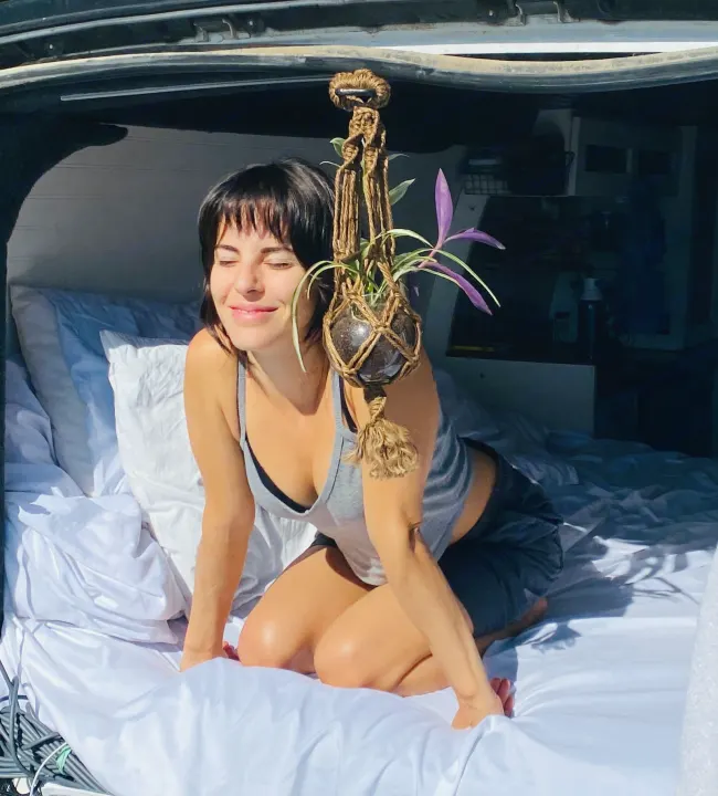 Woman smiles in her comfortable RV rental bed, bathed in sunlight. A peaceful van life moment.. Chevrolet Express 3500 2012