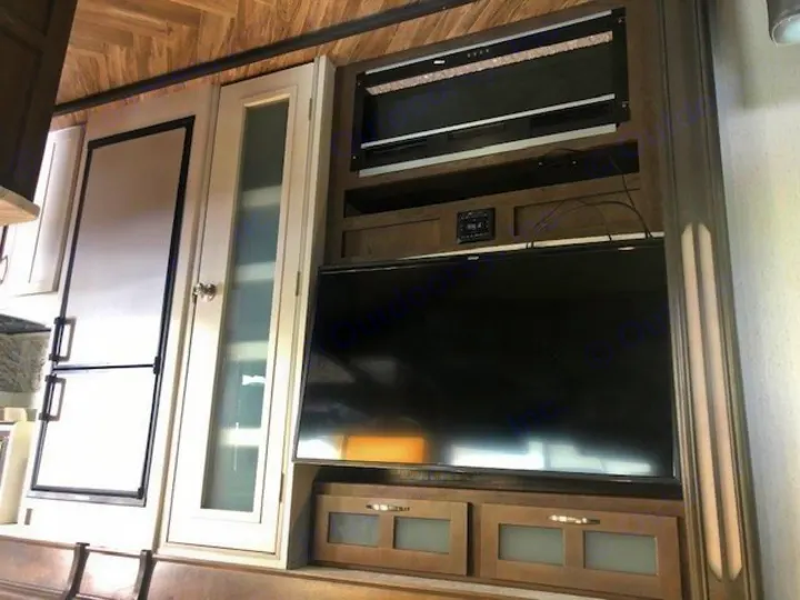 Inside an RV rental: a modern interior with a sleek fridge, entertainment center featuring a TV, and an electric fireplace.. Astoria 1500 2021