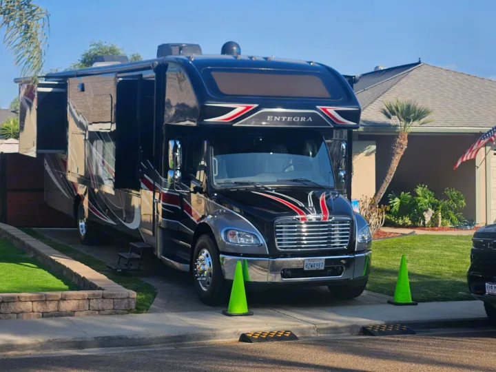 Large black Entegra RV rental with extended slide-outs in a sunny driveway, marked by green cones.. Entegra Coach Accolade XL 2021
