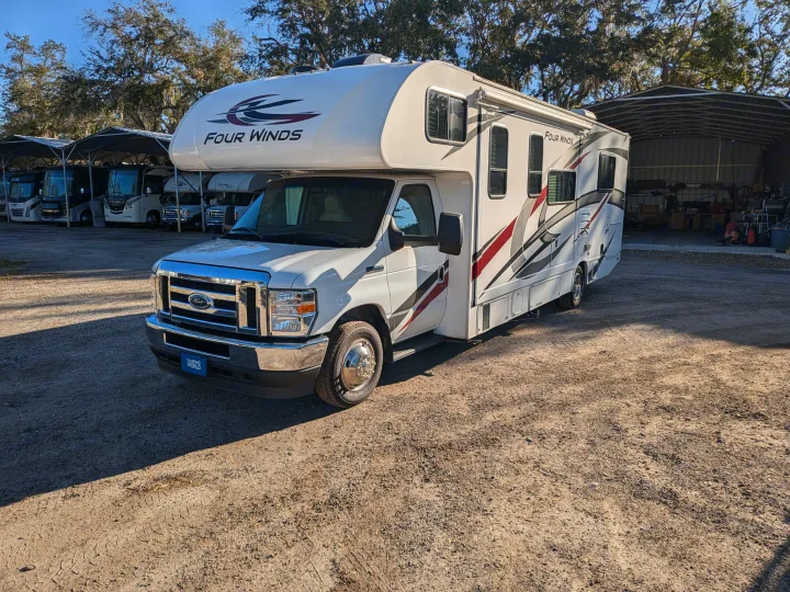White Four Winds Class C RV for rv rental, parked on a sunny lot near shaded RVs and a storage building.. Thor Motor Coach Four Winds 2022