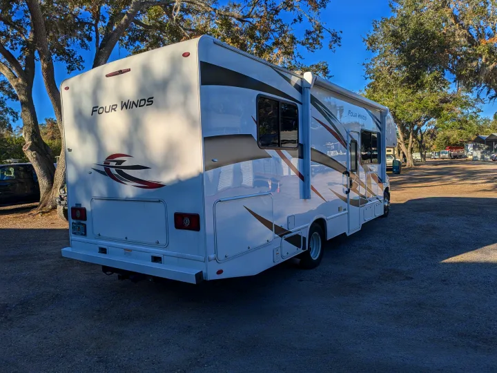 A white Four Winds Class C RV rental gleams in the sun on a gravel lot, ready for your next outdoor adventure.. Thor Motor Coach Four Winds 2022