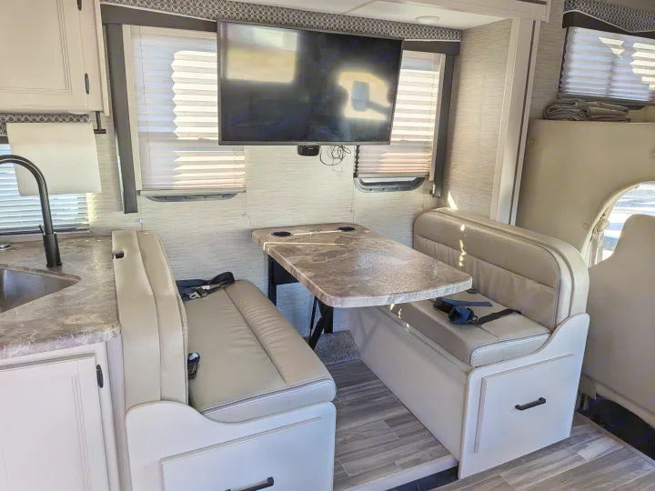 RV rental interior: dinette with table, bench seating & seatbelts, TV, plus a partial kitchen view with sink.. Thor Motor Coach Four Winds 2022