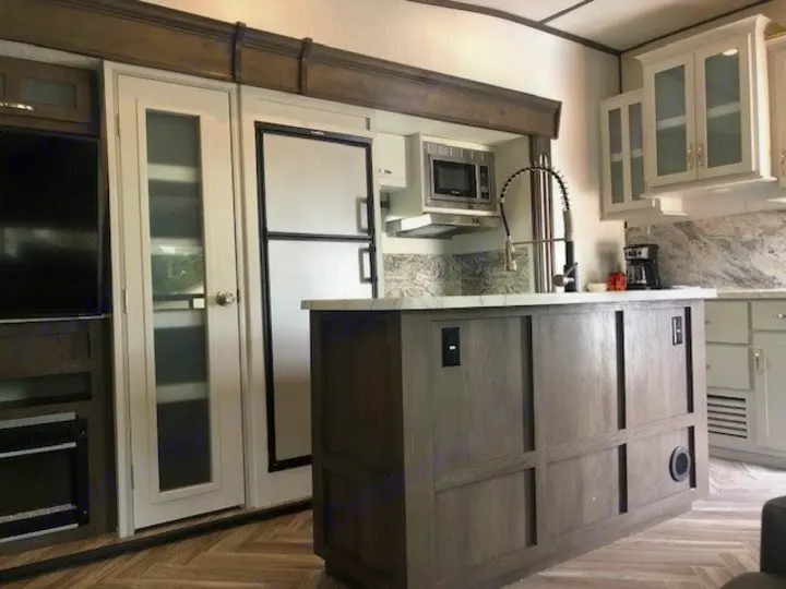 This RV rental kitchen features an island, modern appliances, white cabinets, and living area access, with stylish flooring.. Astoria 1500 2021