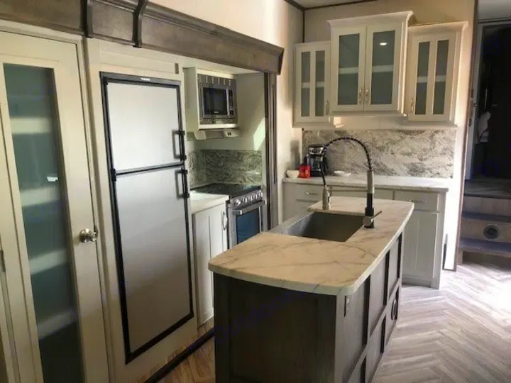 Modern RV rental kitchen interior featuring an island, full fridge, and stylish marble counters.. Astoria 1500 2021