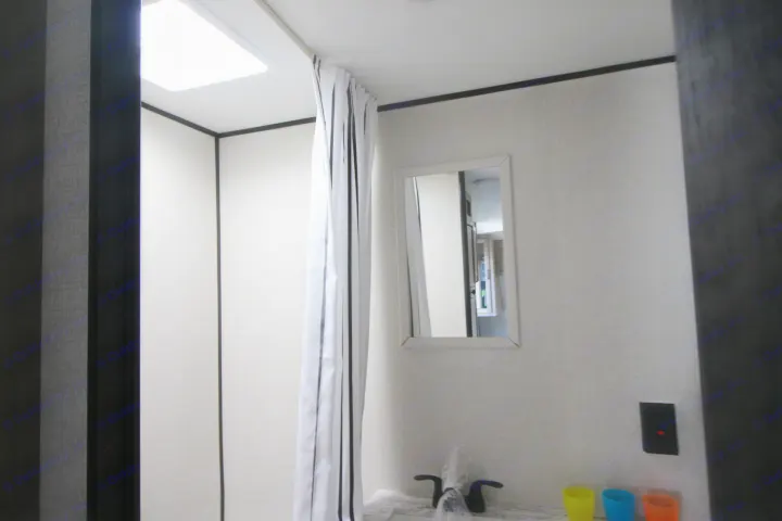 This RV rental bathroom features a shower with a striped curtain, a sink with colorful cups, a mirror, and bright overhead light.. Starcraft Autumn Ridge 180BHS 2023