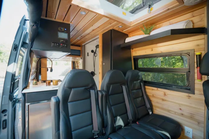 This modern RV rental showcases a bright interior with wood paneling, sleek kitchen, plush seating, and a compact shower.. Mercedes Sprinter 2023