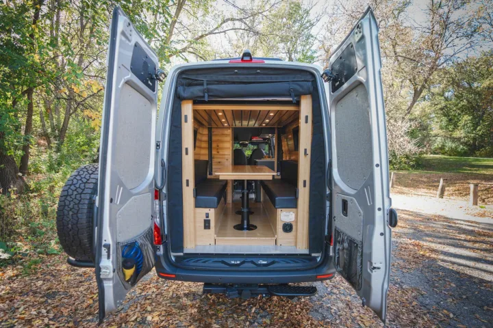 View inside a custom RV rental van: wooden interior, dining table with benches, ready for adventure.. Mercedes Sprinter 2023