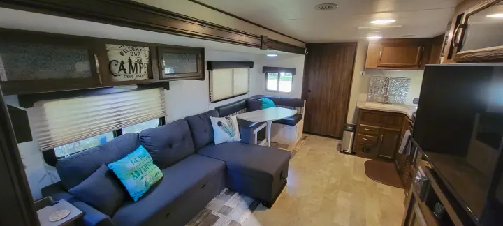 Cozy RV rental interior showing a comfortable L-shaped sofa, dining booth, and functional kitchen space.. Coachmen Apex 265rbss 2019