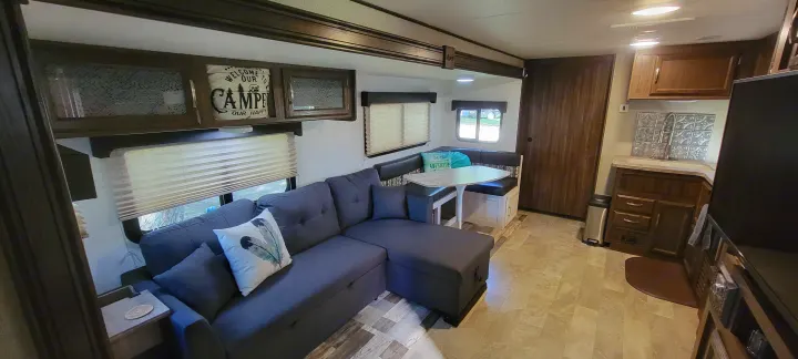 Comfortable RV rental interior with a spacious gray sectional, dining booth, and full kitchenette. Your adventure awaits!. Coachmen Apex 265rbss 2019
