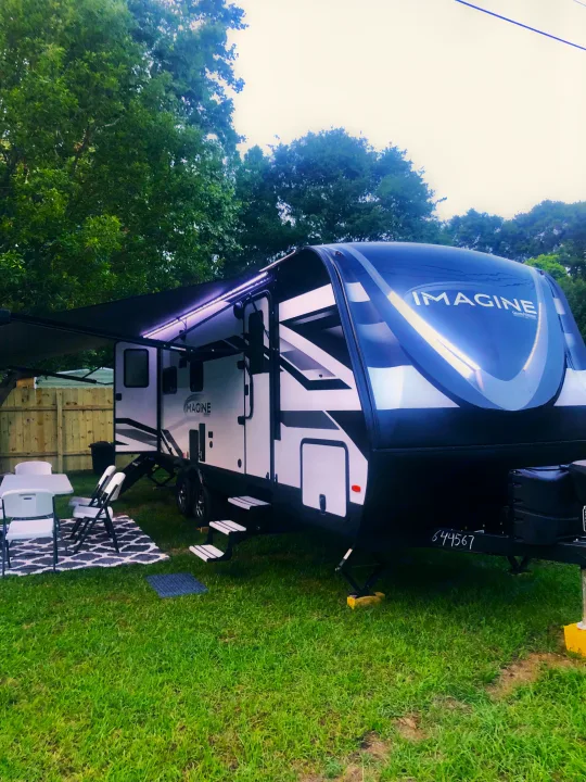 Modern RV rental set up with an illuminated awning & outdoor seating on grass. Perfect for camping trips.. Grand Design Imagine 2023