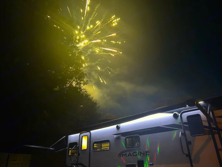Night sky ablaze with fireworks over a lit-up RV rental, perfect for a festive camping trip.. Grand Design Imagine 2023