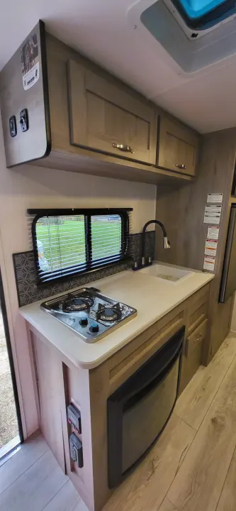 Experience comfort in this RV rental's modern kitchenette, featuring a two-burner stove, sink, and sleek cabinets.. A Liner Ascape 2024