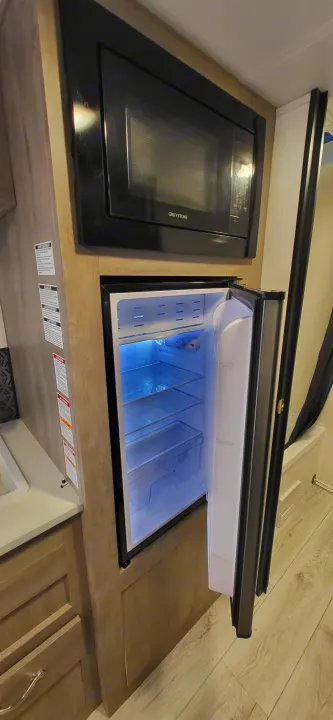 RV rental kitchen showcasing a Greystone microwave, and an open, illuminated compact refrigerator within wood cabinetry.. A Liner Ascape 2024