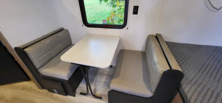 Cozy RV rental interior featuring a bright dinette area with two benches and a table, ideal for meals or work on the road.. A Liner Ascape 2024