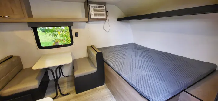 This rv rental interior features a functional dinette, window, AC unit, and a comfortable sleeping area with a gray bed.. A Liner Ascape 2024