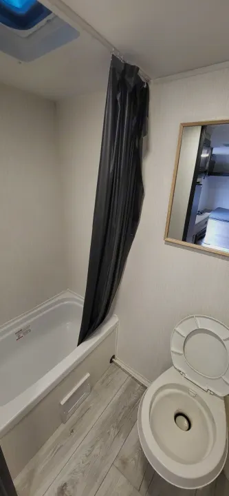 Inside a compact RV rental, this bathroom features a tub with a black shower curtain, toilet, and mirror reflecting the bedroom.. A Liner Ascape 2024