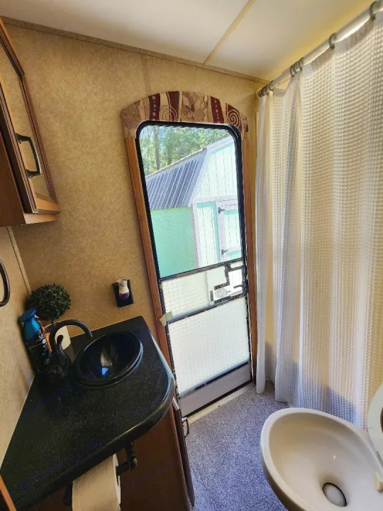 RV rental's compact bathroom: sink, toilet, and shower with a view of a shed through the door.. Crossroads RV Cruiser 2012