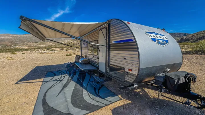 This RV rental travel trailer is set up with an extended awning, chairs, and mat, perfect for desert camping adventures.. Forest River Salem FSX 2020