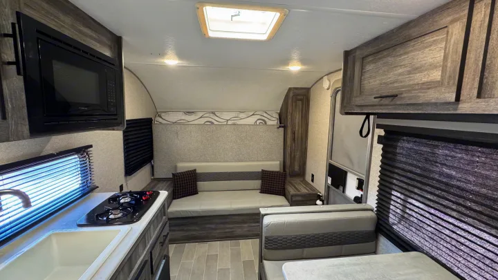 This RV rental interior features a modern kitchen with a microwave & stove, sofa seating, and a dinette with a table.. Forest River Salem FSX 2020