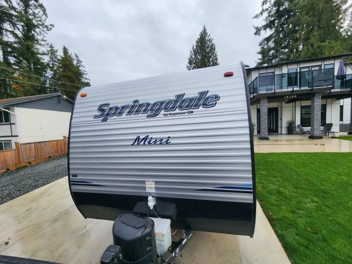 Springdale Mini RV rental, a grey and white travel trailer, parked on a concrete driveway, ready for your adventure.. Keystone RV Springdale 2018