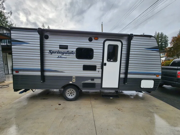 Side view of a compact grey Springdale Mini travel trailer rv rental on a concrete driveway. Ready for your camping adventures!. Keystone RV Springdale 2018