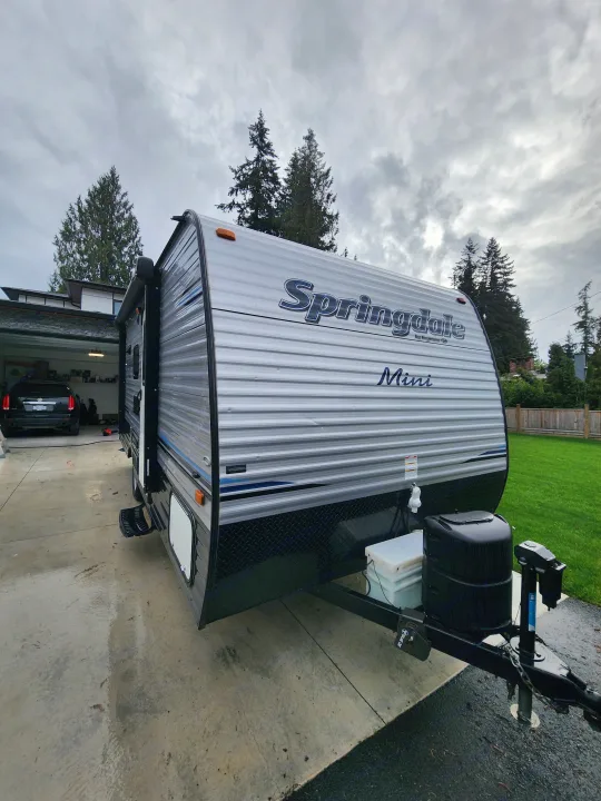 Silver Springdale Mini travel trailer, ideal for your next RV rental, parked on a wet driveway under cloudy skies.. Keystone RV Springdale 2018