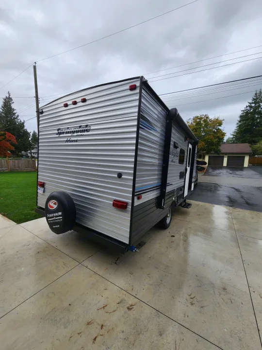 A Springdale Mini RV, ideal for your next rv rental trip, is parked on a wet driveway under a cloudy sky.. Keystone RV Springdale 2018