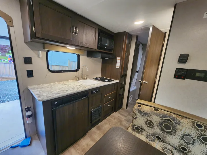 Inside this RV rental: A compact kitchen with a sink, stove, microwave, and fridge, ready for your travel adventures.. Keystone RV Springdale 2018