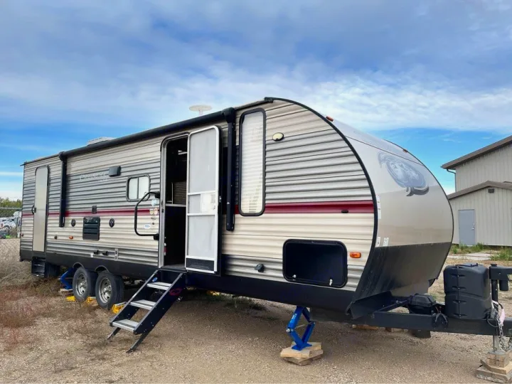 Spacious travel trailer RV rental parked outdoors, ready for adventure. Features an open door with steps and leveling jacks.. Forest River Cherokee 2018