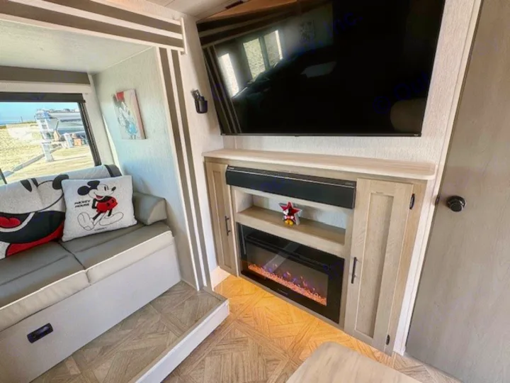 Inside an RV rental: Relax on the Mickey Mouse sofa, watch TV, and enjoy the ambiance of the electric fireplace.. Forest River Wildwood 2024