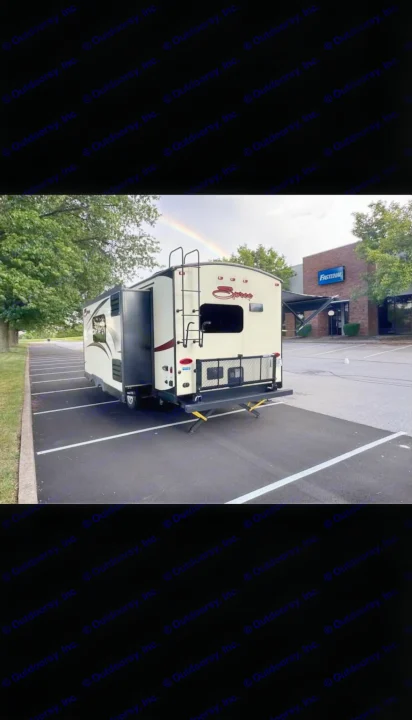 Travel trailer RV rental with extended awning in a parking lot, a rainbow visible overhead. Fastenal building nearby.. KZ Spree 2017
