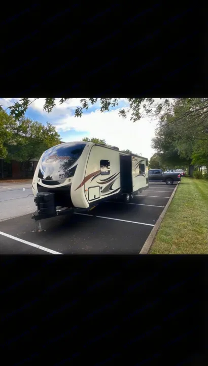 Spacious cream travel trailer (RV rental) with slide-out, parked in a lot under trees.. KZ Spree 2017